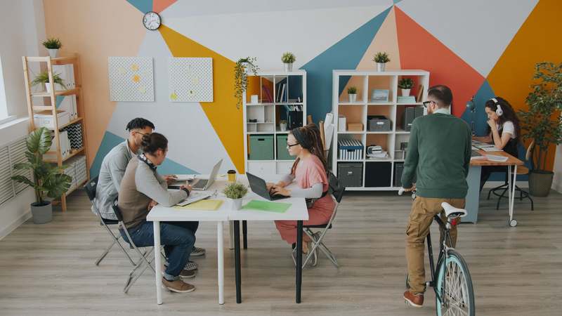 Diverse entrepreneur team reviewing business metrics on laptop and whiteboard in modern co-working space